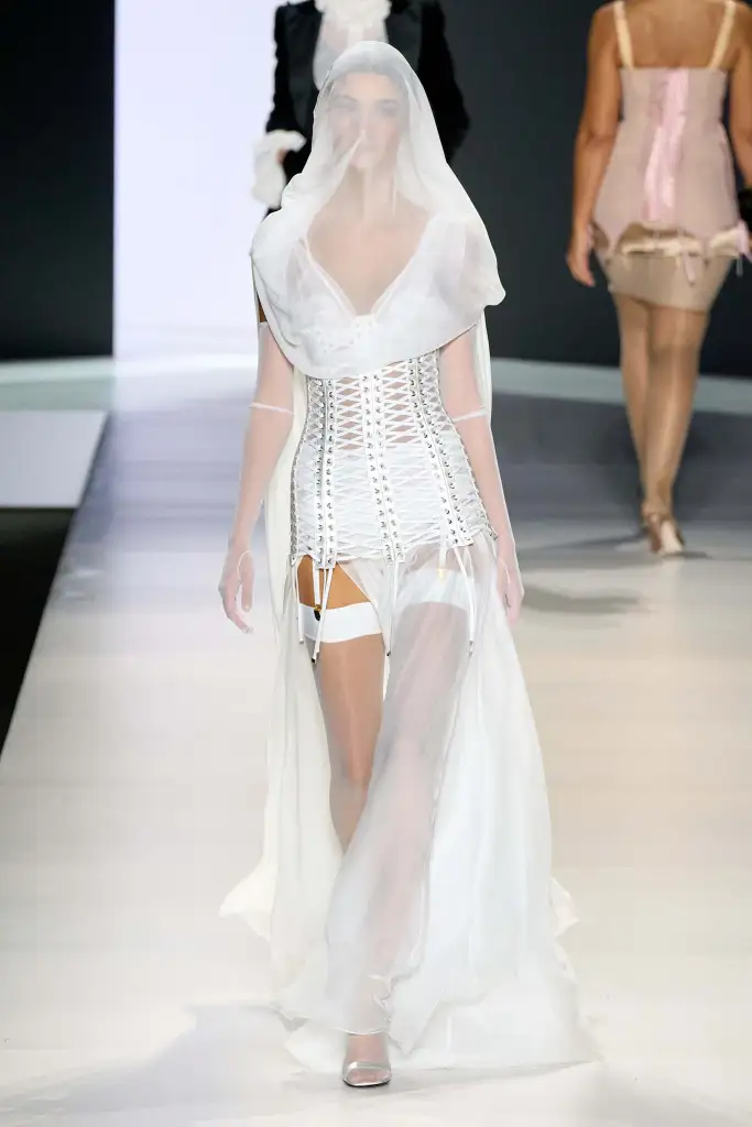 Este aproape imposibil să desprinzi firul subțire dintre arhiva seducătoare a anilor '90 a casei Dolce & Gabbana și explozia stilului vampy, îndrăzneț și delicios de întunecat care a urmat. Aceste două elemente sunt atât de strâns legate încât formele inspirate de lenjeria intimă au devenit sinonime cu creațiile lui Domenico Dolce și Stefano Gabbana. Pe măsură ce marca se apropie de un moment important – 40 de ani de Dolce & Gabbana – nu este de mirare că duo-ul de designeri se simte nostalgic. Pentru sezonul Primăvară/Vară 2024, brandul și-a dedicat colecția vixenilor, sirenlor și femeilor fatale multifacetate care au modelat identitatea luxoasă a casei de modă de aproape patru decenii. Intitulată "Femei", panoplia de lenjerie senzuală Dolce & Gabbana este un omagiu adus esenței feminității; frumusețea carnală innată și misterul puternic exprimat prin sensibilitatea budoarului. Pentru o colecție ce celebrează feminitatea, Dolce & Gabbana a adunat un impresionant alai de modele pentru a reflecta ceea ce ei consideră a fi emblematic pentru ADN-ul lor. Naomi Campbell, Ashley Graham, Vittoria Ceretti, Stella Maxwell și Irina Shayk au îmbrățișat toate modul inerent flirtez al îmbrăcămintei italiene, fie în lenjerie tehnică transparentă, fie prin reinterpretarea pieselor clasice bine croite. Evocând o uniune între inocență și maturitate, D&G pare să fi făcut referire la colecția lor provocatoare Primăvară/Vară 1992 într-o colecție care lasă puțin loc imaginației – sau a lăsat puțin pe mood board. Acest concept de forță inerentă găsită în formele erotice a continuat și în afara podiumului, în primul rând, unde invitații au determinat expresia sexualității lor fie prin extravaganță, impertinență sau modestie. Și, deși unele rapoarte susțin că spectacolul a început cu 45 de minute întârziere – se zvonește că întârzierea Kylie Jenner a întârziat spectacolul, rezultând în piesa "What Was I Made For?" a Billie Eilish rulând în buclă aproape o oră – show-ul a fost o editare precisă. Aderent pe corp, precis în execuție și un nod strâns care îmbină renașterea anilor '90 a Dolce & Gabbana cu prezentul.